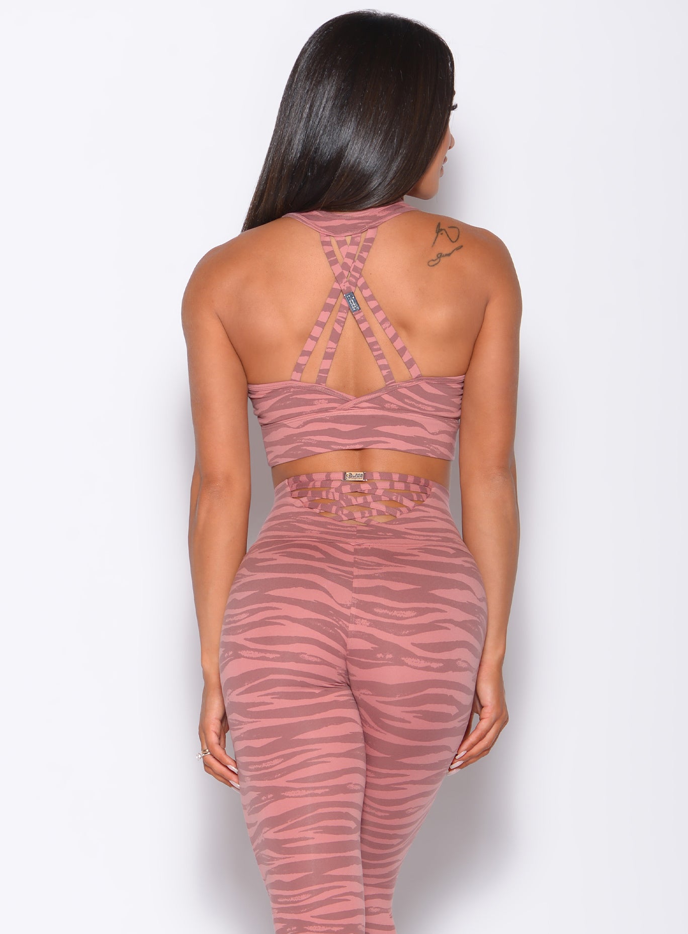 Back profile view of a model wearing our rival sports bra in nude blush color and a matching sexy back leggings in tiger print