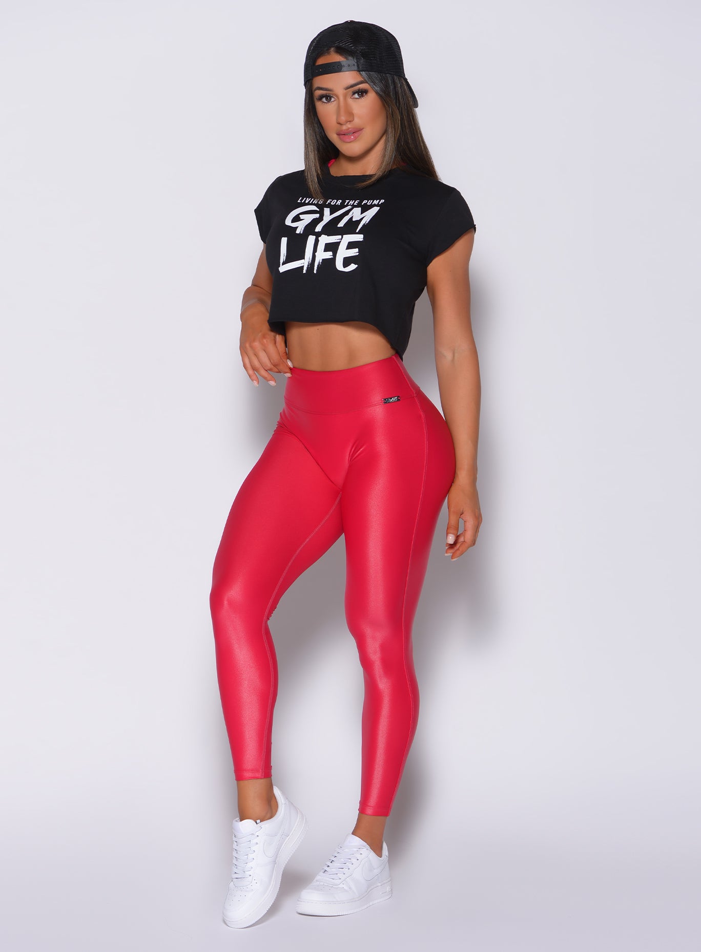 Front profile view of a model wearing our gloss leggings in red color and a black top