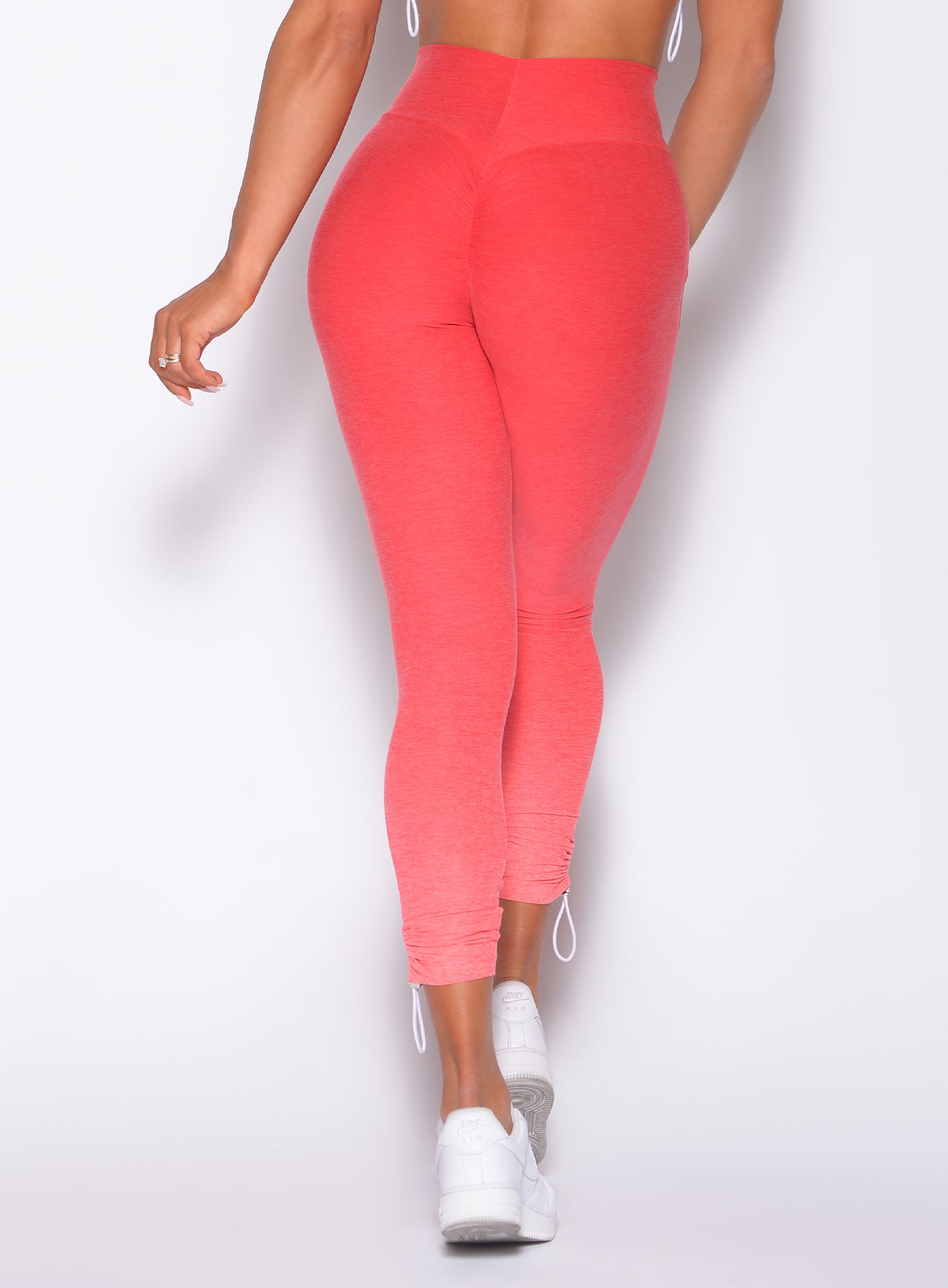 Zoomed in back side picture of our toggle leggings in profile view of a model in our toggle leggings in Ombre Fiji Coral and a matching bra