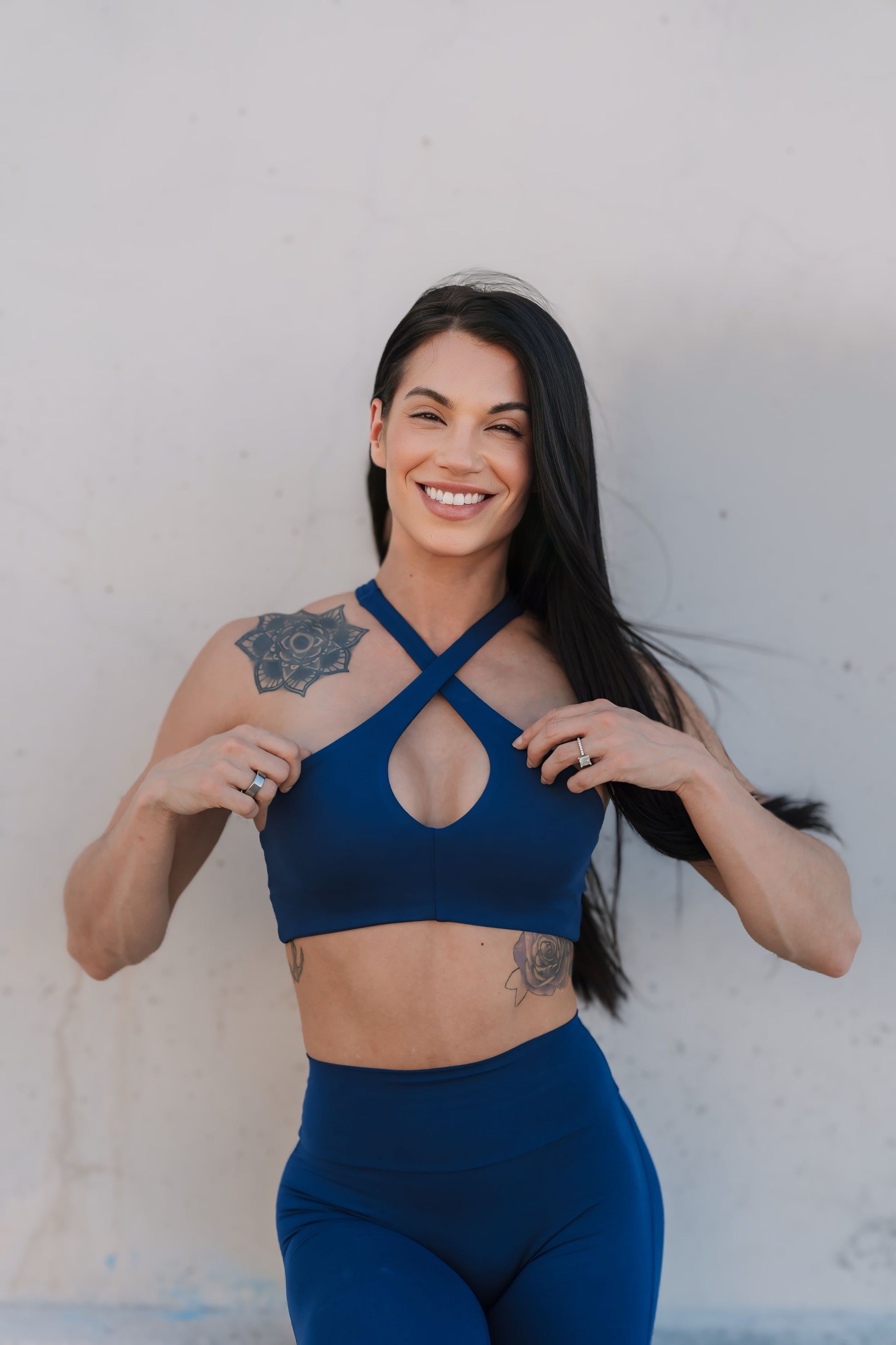 Front profile of model standing against a wall wearing our Cross Over Halter Bra and the matching leggings in Royal Indigo color