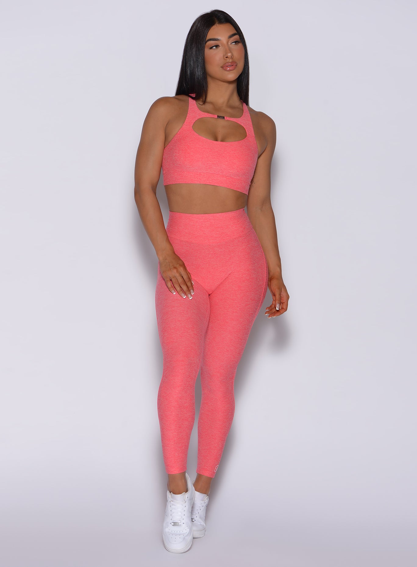 Front profile view of a model in our Pocket Pop Leggings in papaya color and a matching bra