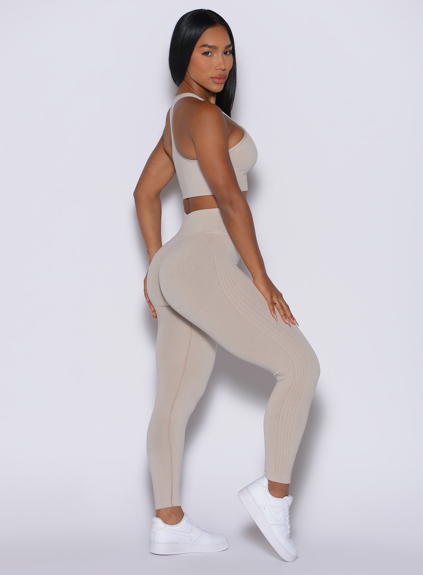 Right side view of a model facing to her right wearing our Contour Seamless Leggings and the matching Lifter Heather Seamless Bra in Oat color