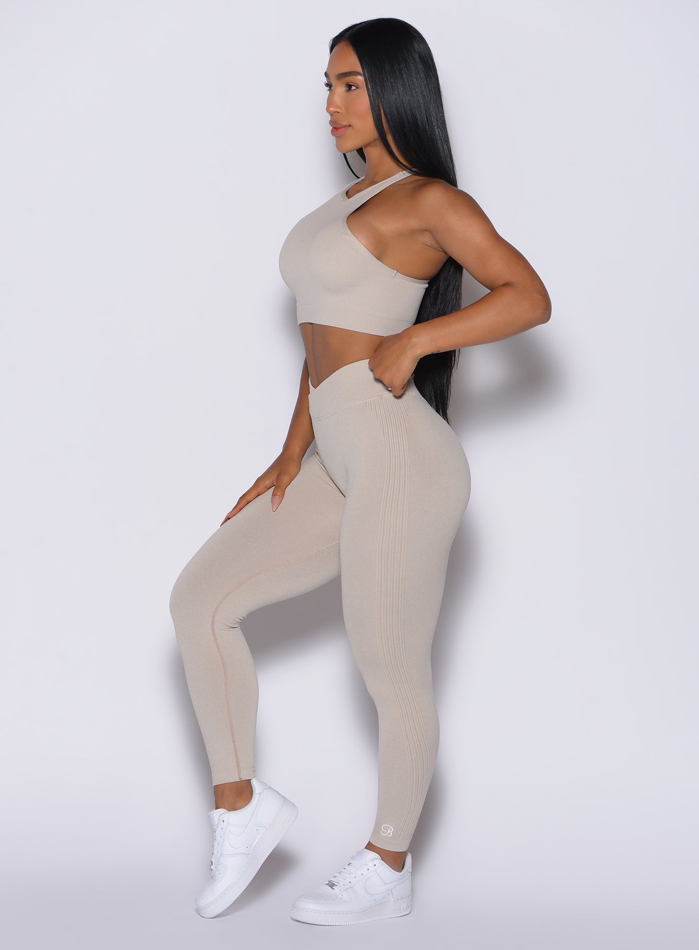 left side profile view of a model facing forward wearing our Contour Seamless Leggings and the matching Lifter Heather Seamless Bra in Oat color