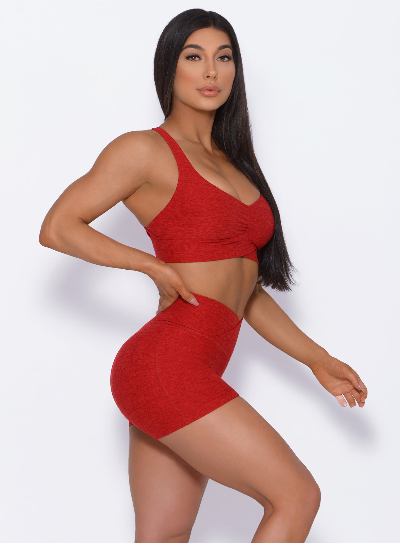 Right side profile view of a model angled right wearing our Tiny Waist Shorts in Sunset Red color and a matching sports bra