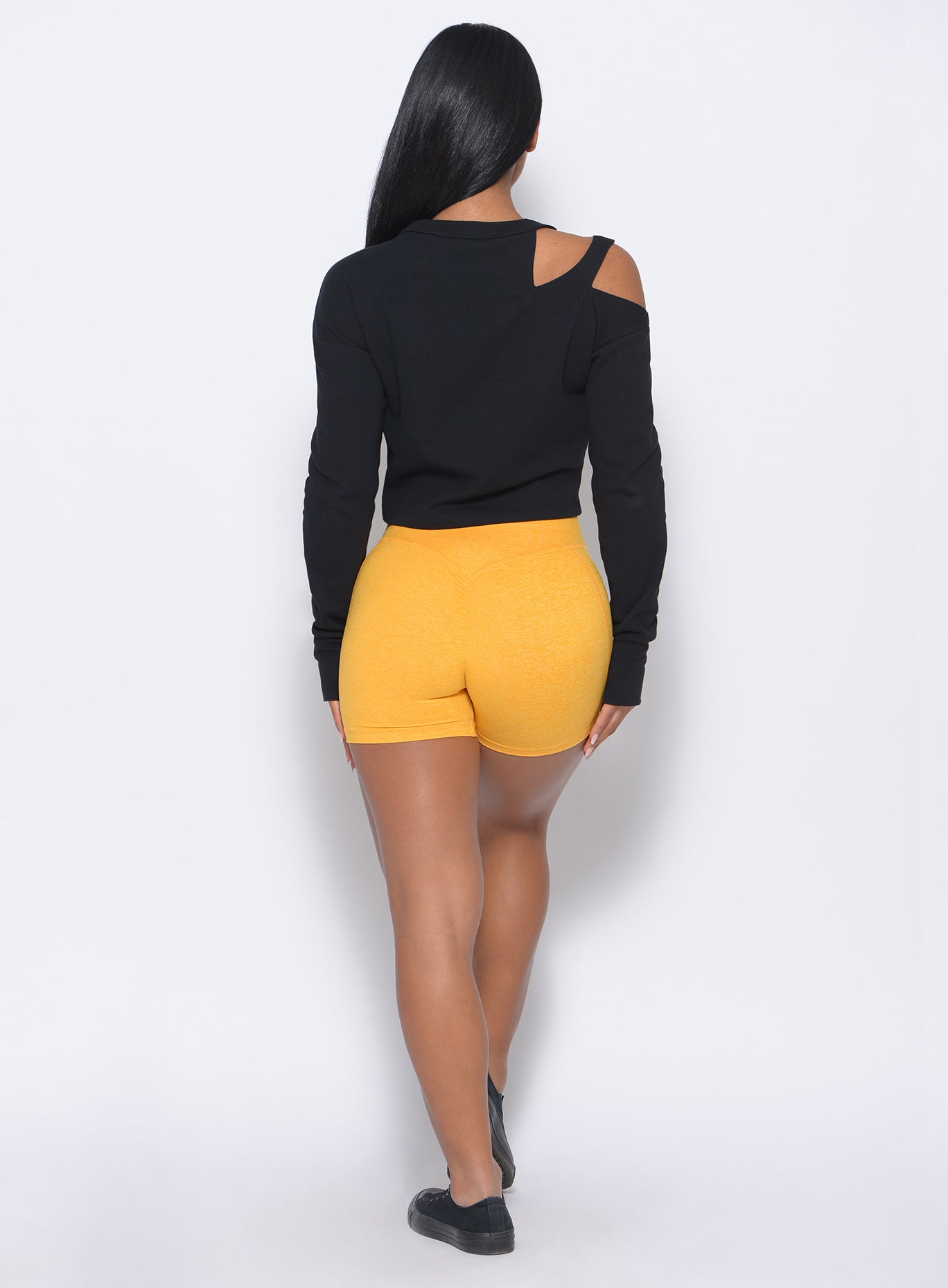 Back profile  view of the model in our tiny waist shorts in sunkissed color and a black pullover