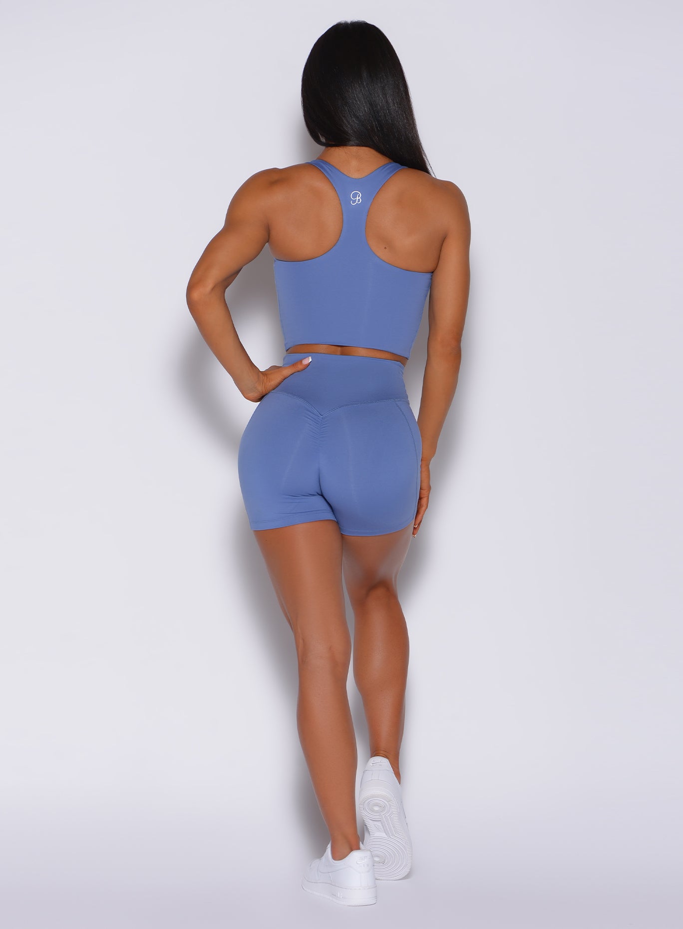 Back profile view of a model in our tiny waist shorts in denim blue color and a matching bra